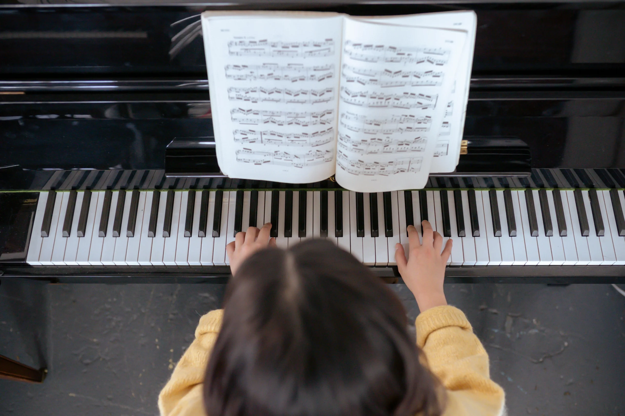 Child's hands playing piano with beginner sheet music visible
